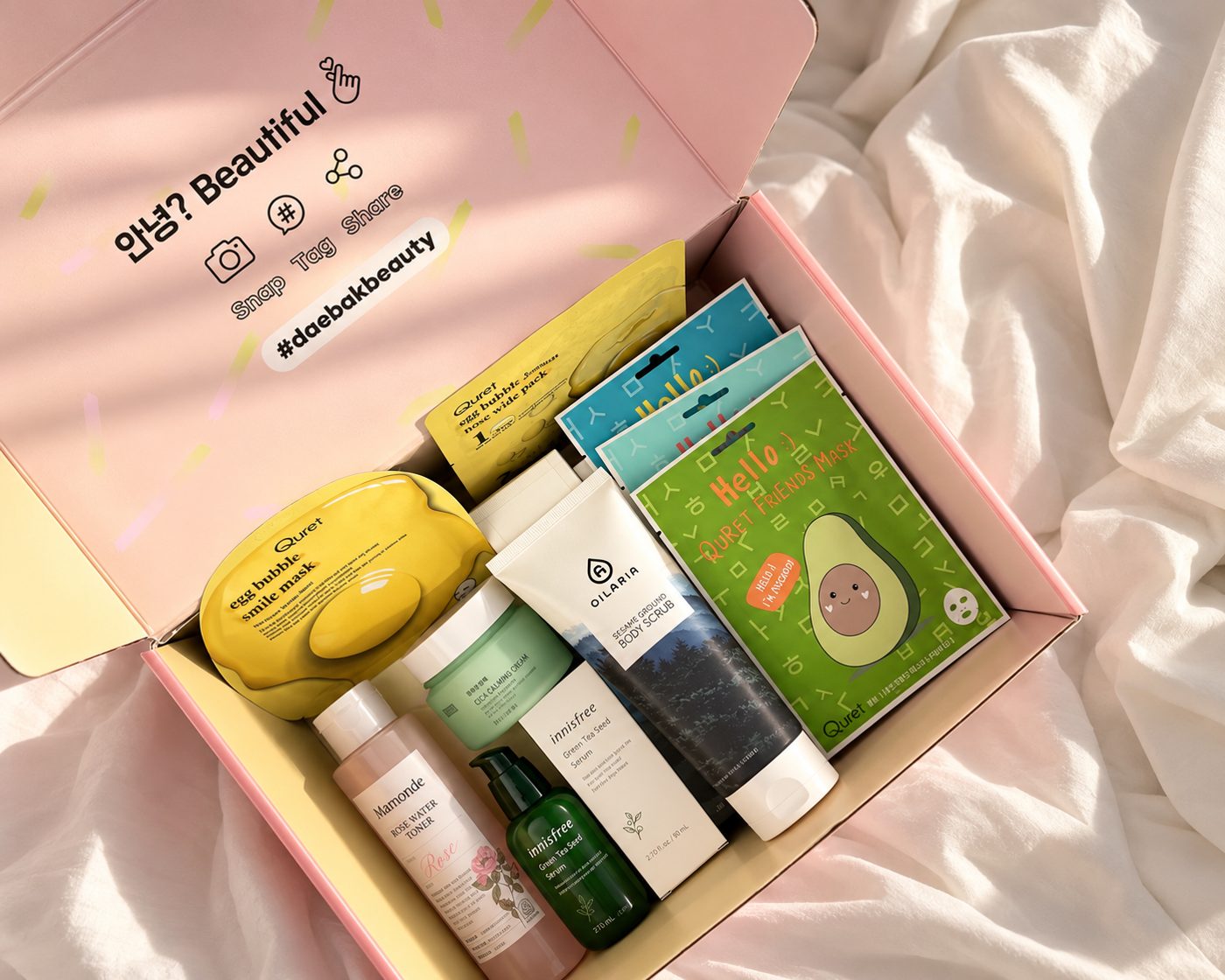An open pink Daebak Beauty box filled with K-beauty products: toner, serum, moisturizer, body scrub, face masks and more