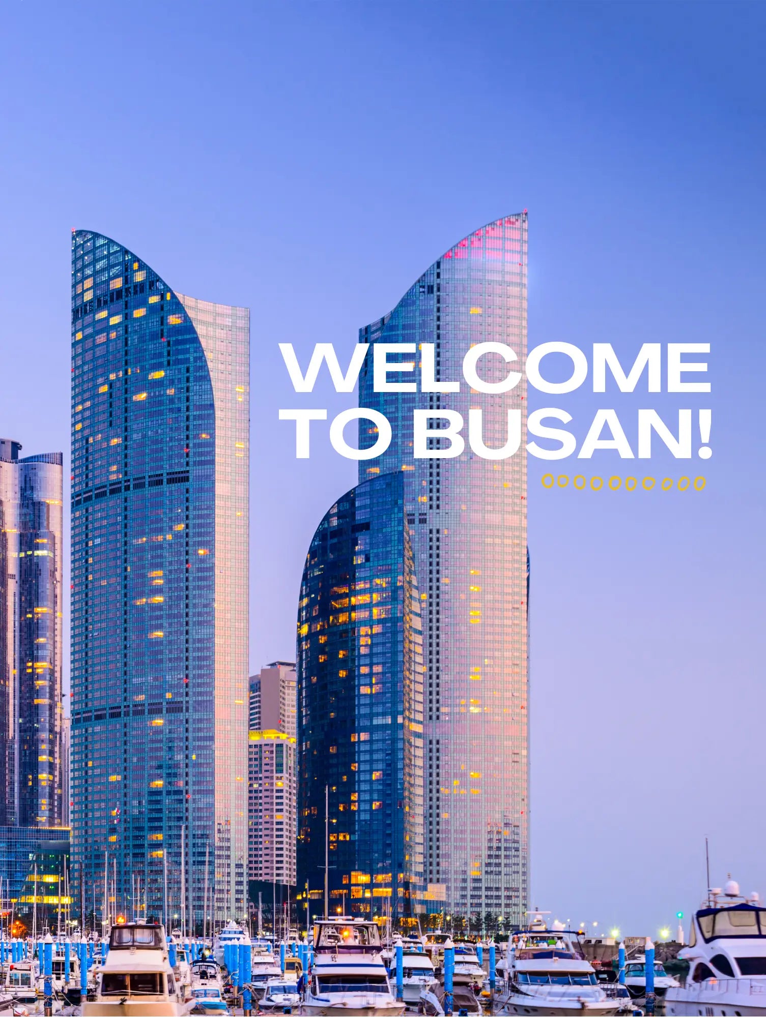 Modern skyscrapers with 'Welcome to Busan!' text against a blue sky.