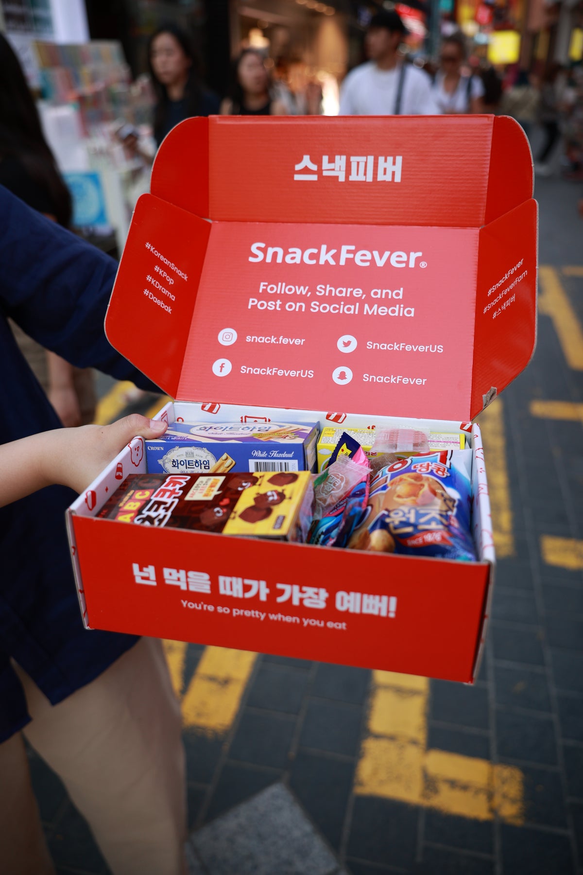 A Snack Fever box held open on a busy Seoul street