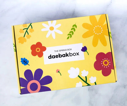 Daebak Spring Box featuring a curated selection of Korean beauty, fashion, snacks, and lifestyle items in bright, seasonal packaging.